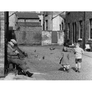  Boy and Girl Walk Down Street Past Seated Elderly Man 